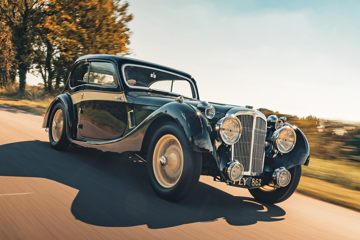 Black pre-war coupe with chrome headlamps on a country road