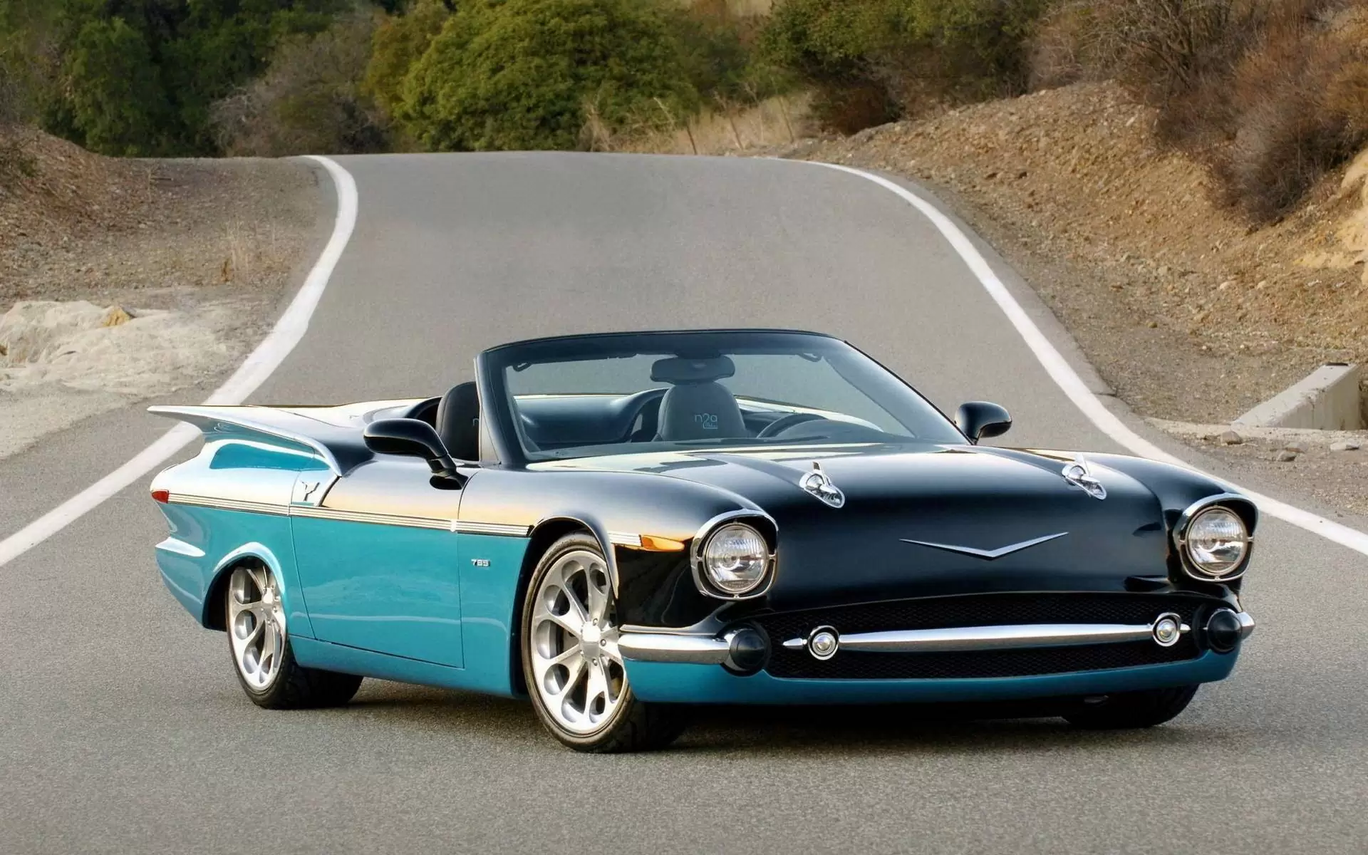 Black and teal custom convertible with tailfins on a winding road